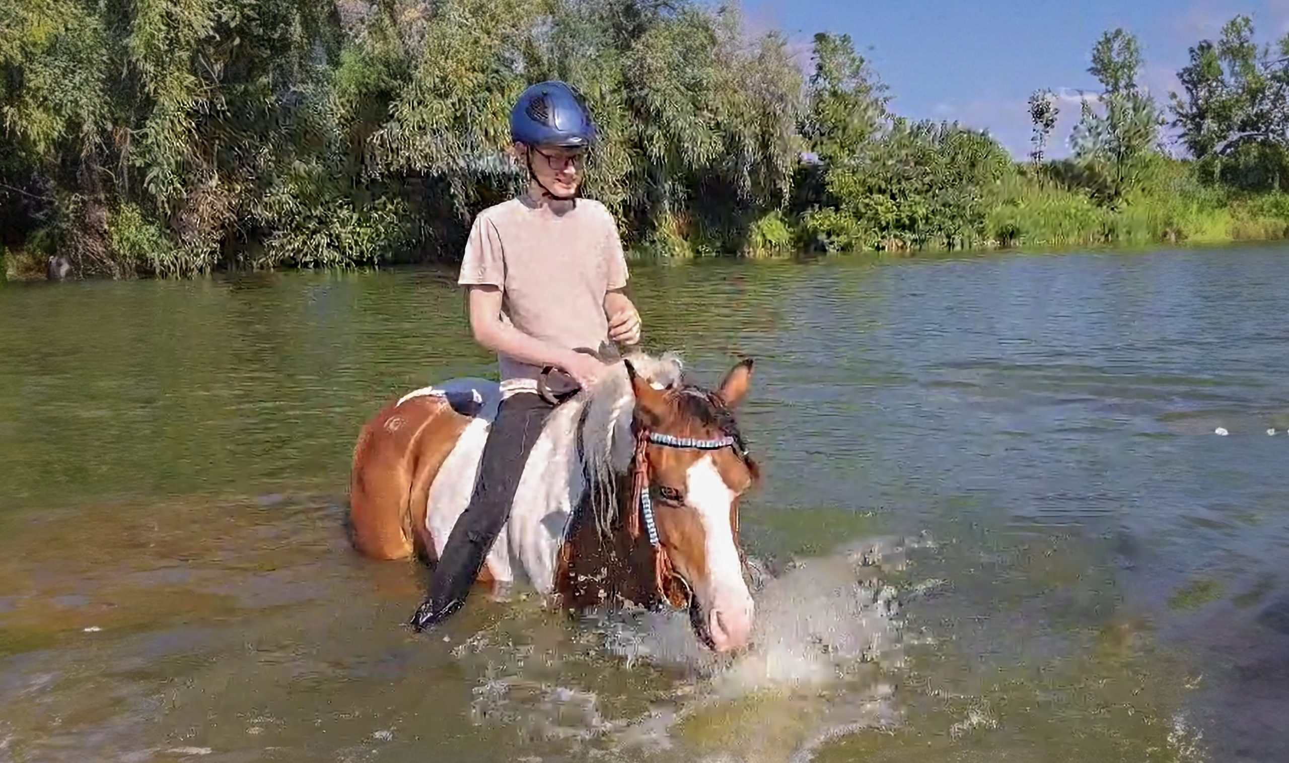 Nelson Ptak sitzt auf einem Pferd. Das Pferd badet in der Mulde, Nelson Ptak lacht.
